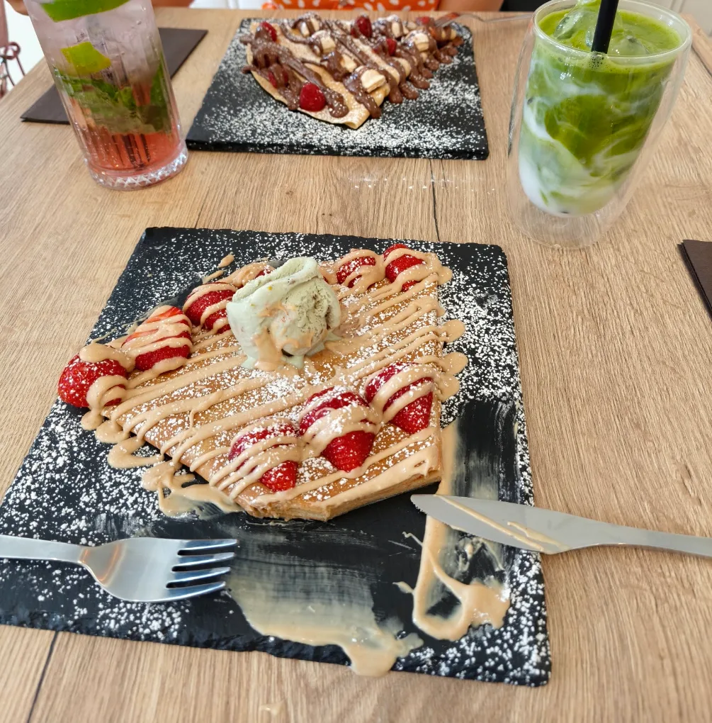 Une gaufre aux fraises, coulis et boule de glace pistache, servie sur ardoise